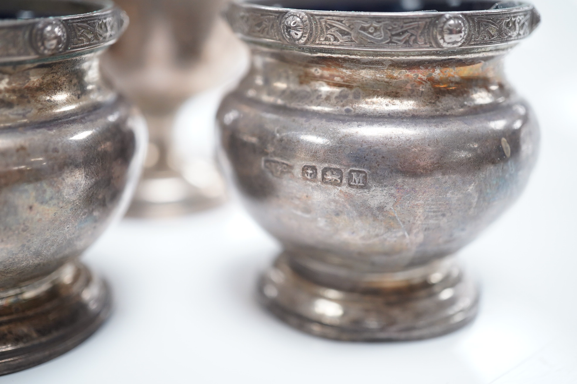 A Victorian repousse silver drum mustard, London, 1887, a silver three piece condiment set, Birmingham, 1936 and a set of three small trophy cups by Mappin & Webb, London, 1925/6. Condition - poor to fair